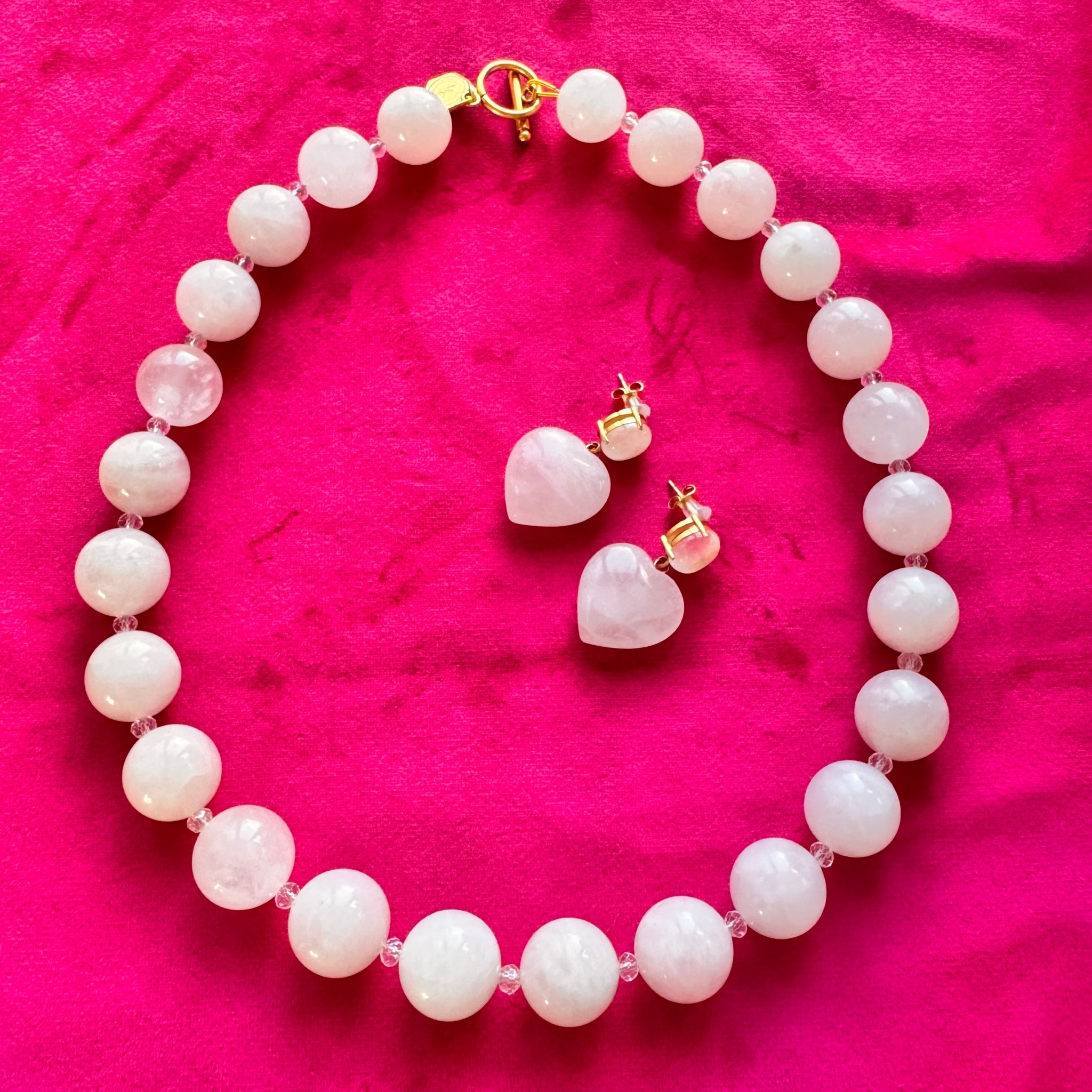 Pearl necklace and heart-shaped earrings on a pink fabric background