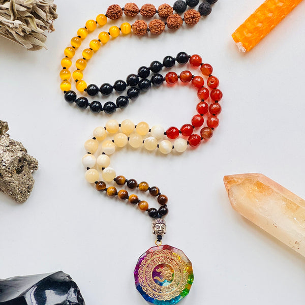 A colorful array of beads with various colors and a central Orgonite OM Symbol Pendant, arranged on a white surface with a crystal and a smudge stick in the background.