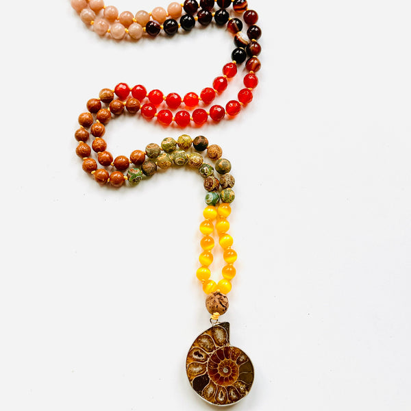 A multicolored beaded mala with a variety of colorful beads and a central ammonite pendant, designed for meditation and personal empowerment on white surface.