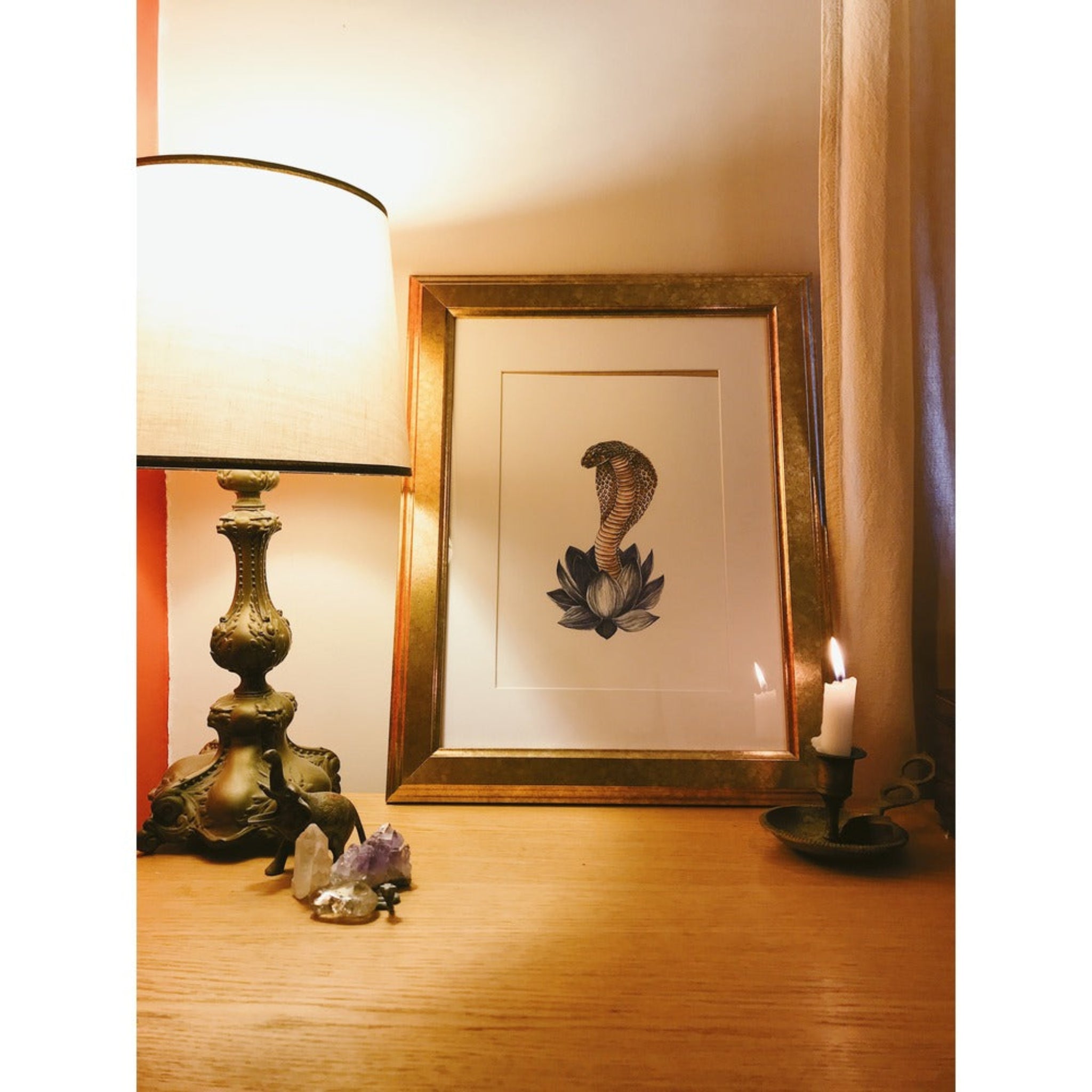Framed artwork on a wall next to a lamp and candle