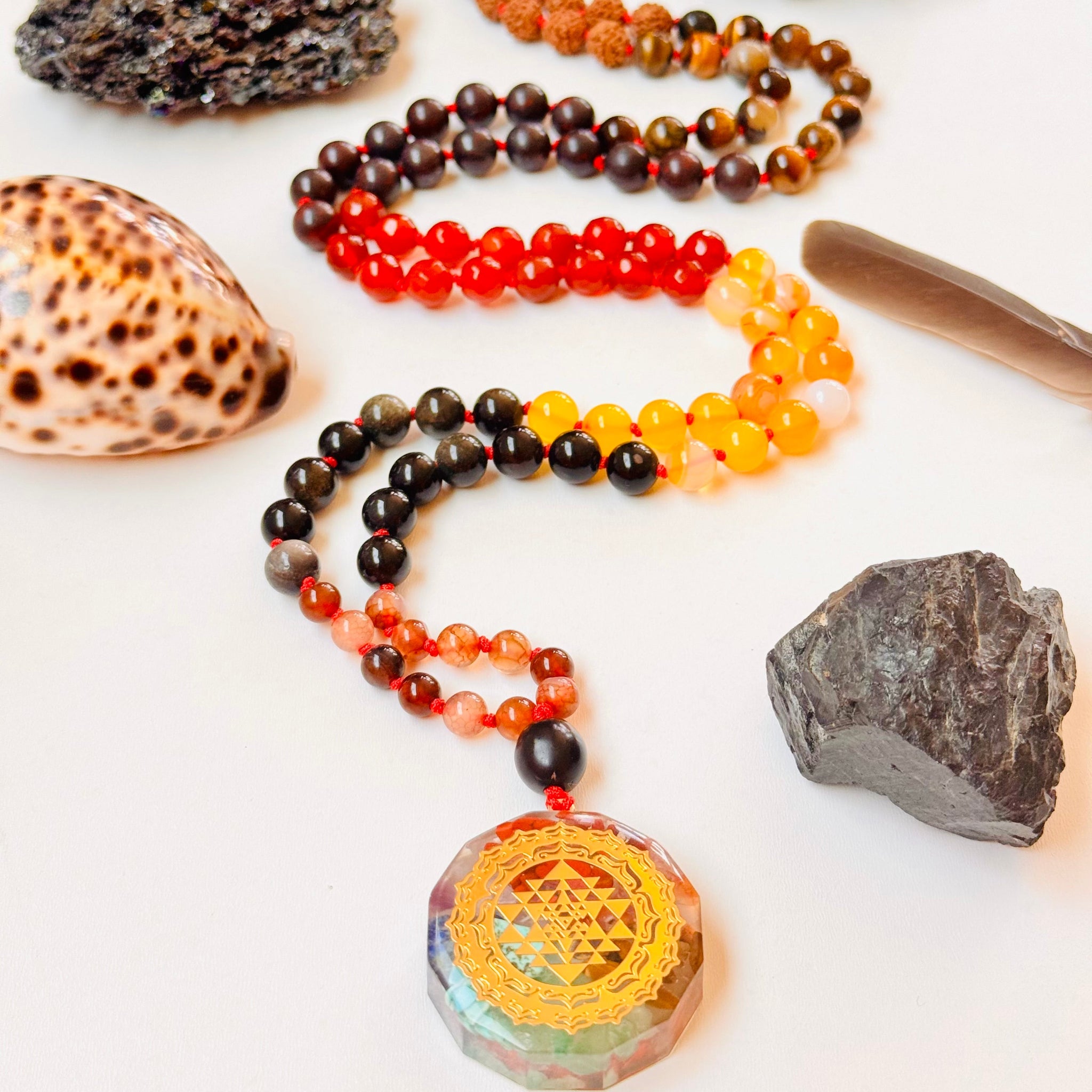 Necklace with multicolored beads and a large pendant on a white surface with rocks and shells.