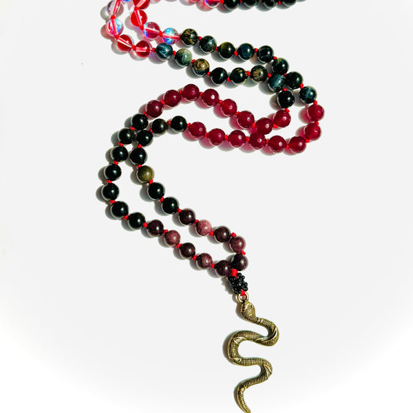 A beaded mala with a variety of colored beads and a brass snake pendant, used for counting mantras or as a meditation aid.