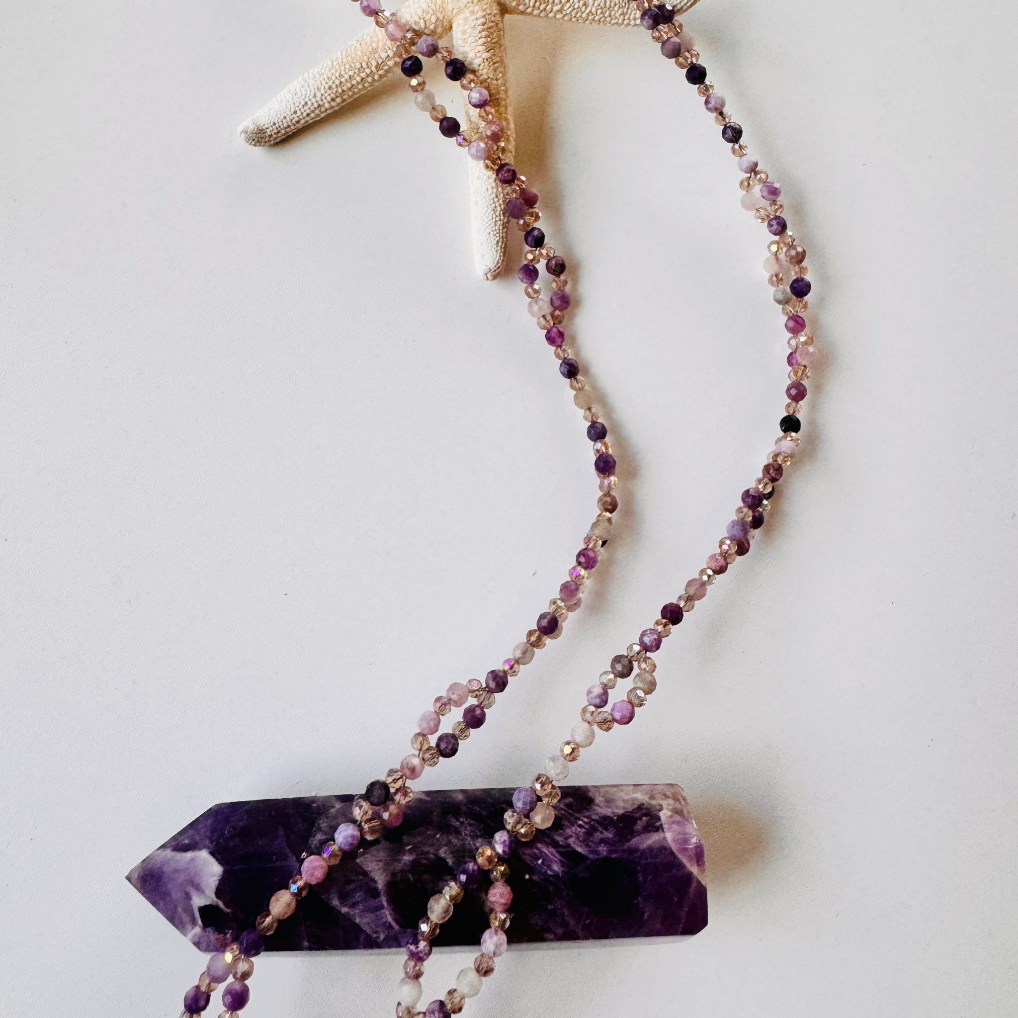 Lepidolite Tantric Necklace on white surface and purple crystal
