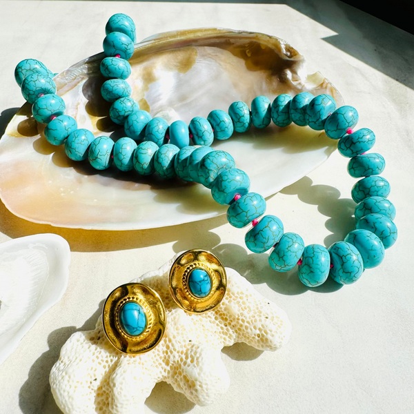 Turquoise beaded bracelet and earrings on a shell with a white background
