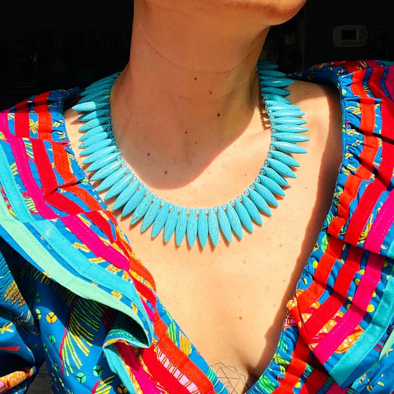 Turquoise spiked necklace worn by a person with colorful clothing.