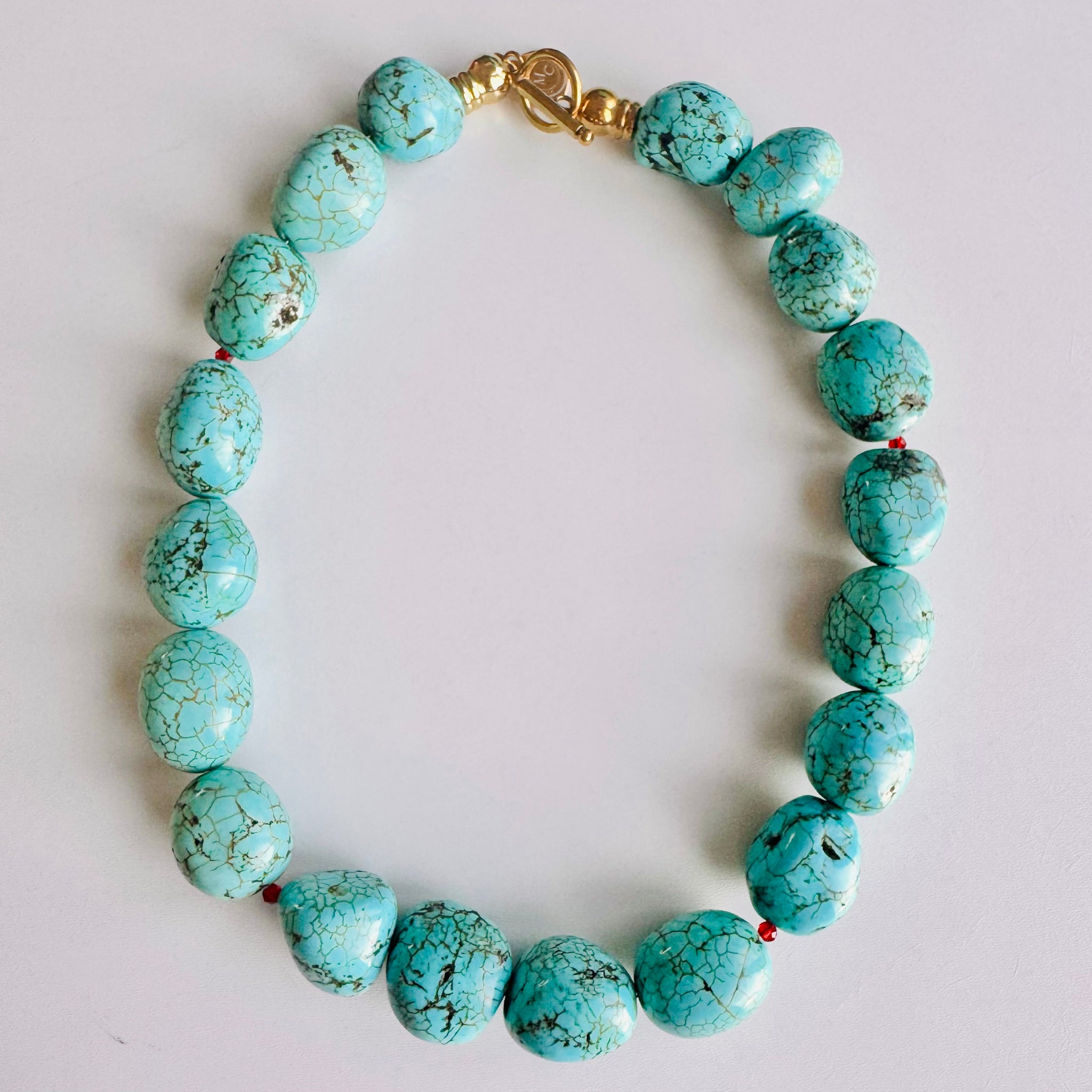 Turquoise beaded bracelet with a gold clasp on a light gray background
