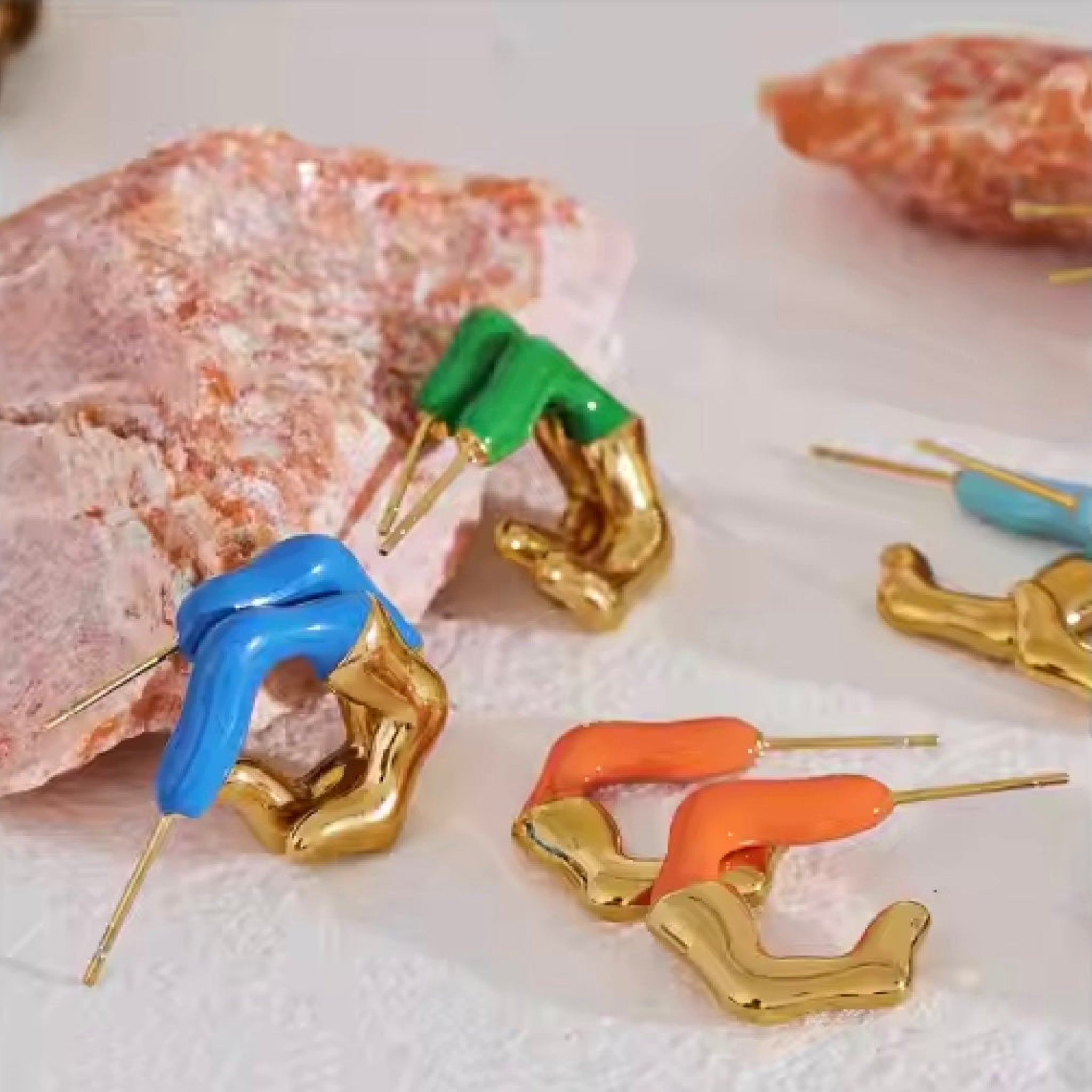 Colorful earrings (blue, orange, green) shaped like hands on a textured surface.