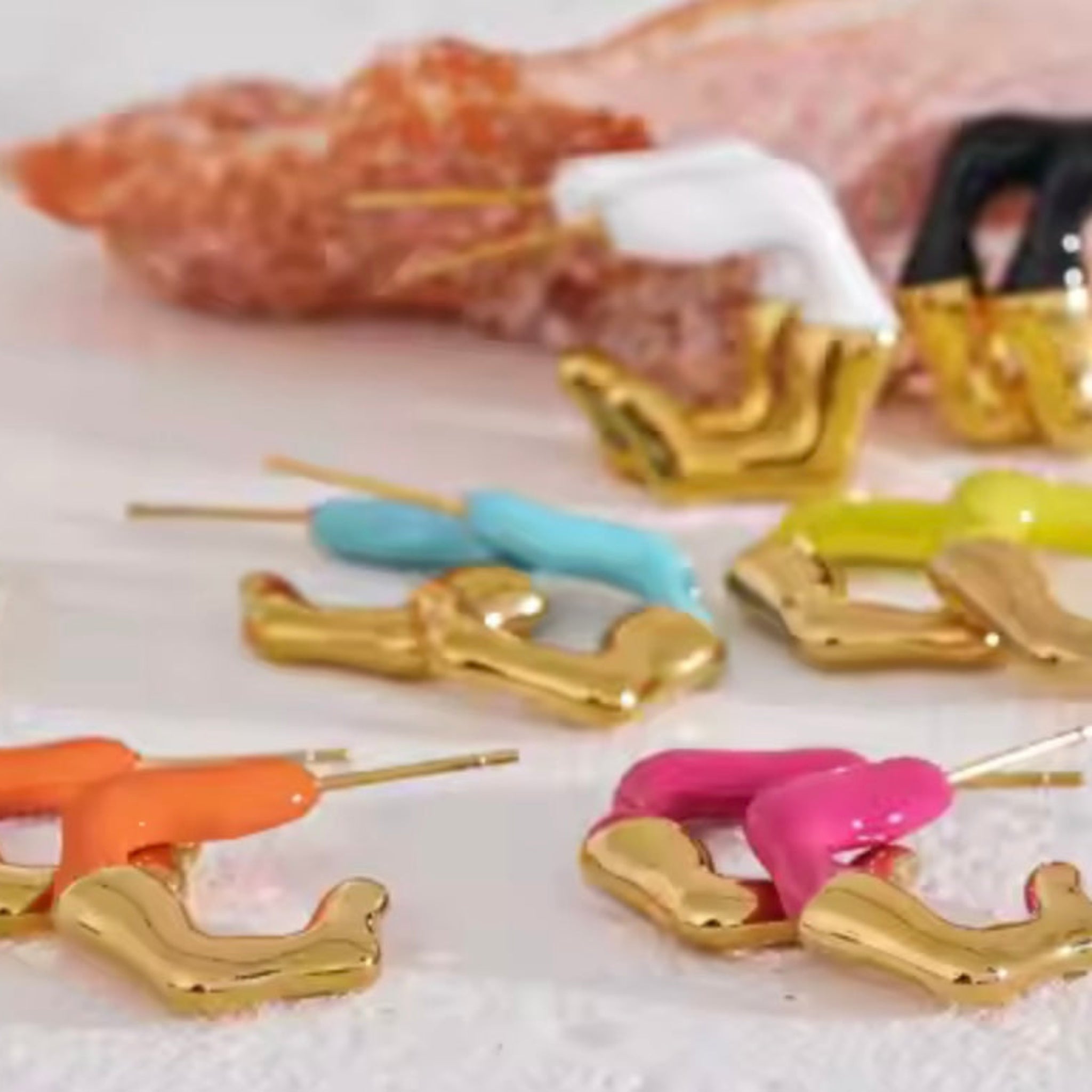Colorful earrings with gold hands holding various objects on a white background.