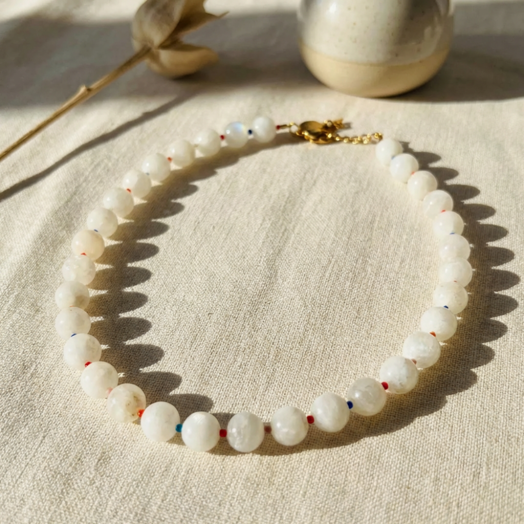 Necklace with white beads and a gold clasp on a beige fabric background