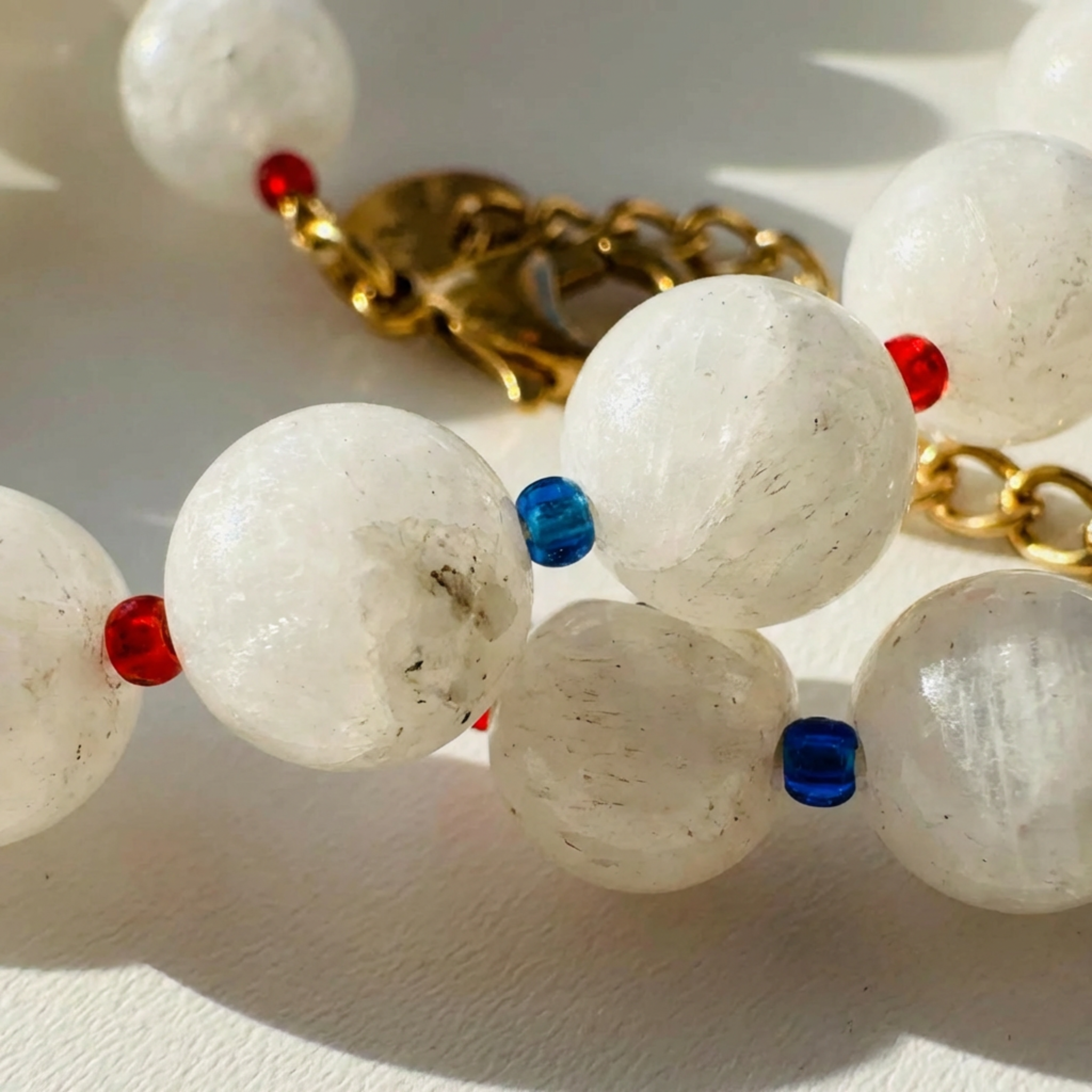 Close-up of a necklace with white beads, red and blue accents, and gold chain.