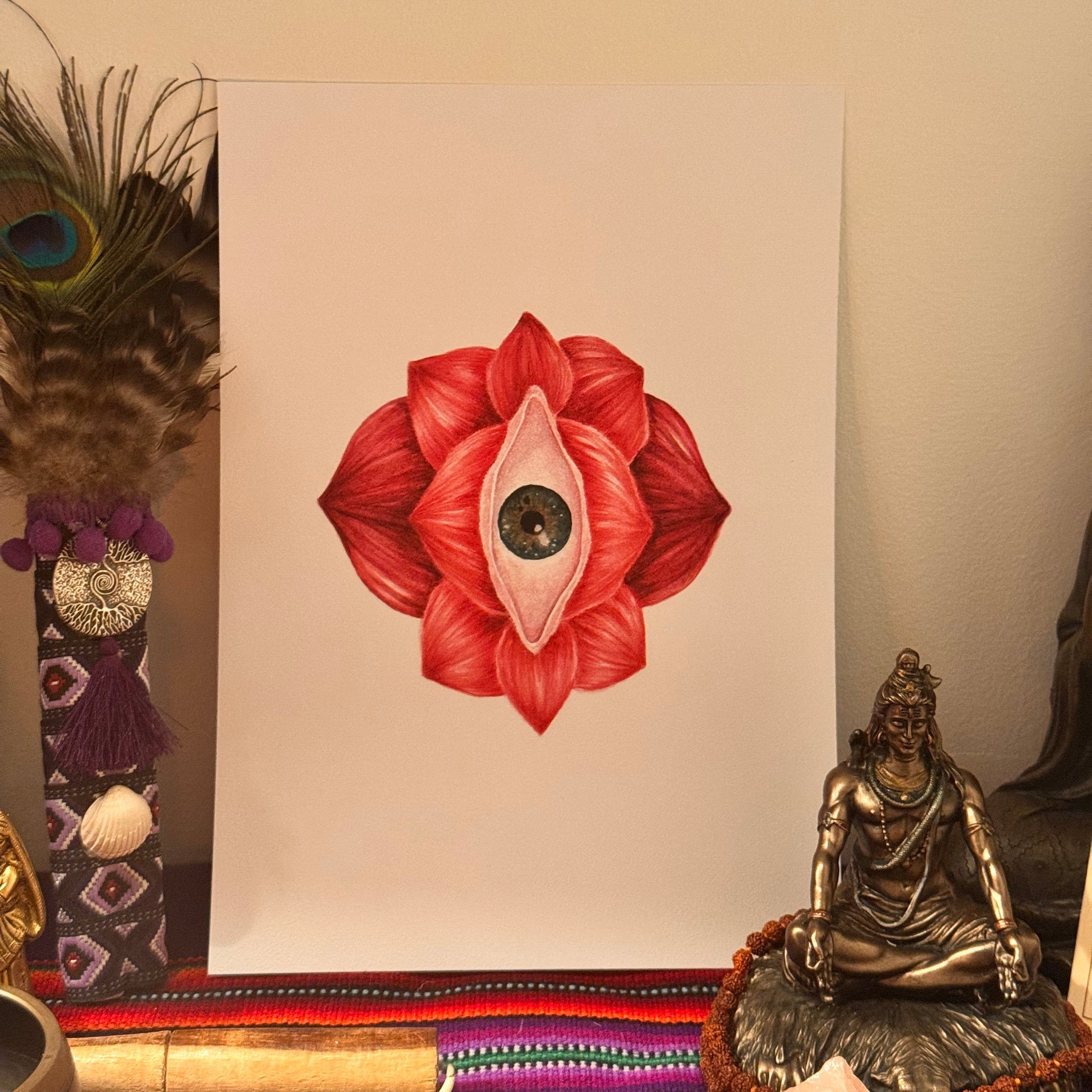 Red flower with an eye design on a white card, surrounded by decorative items.