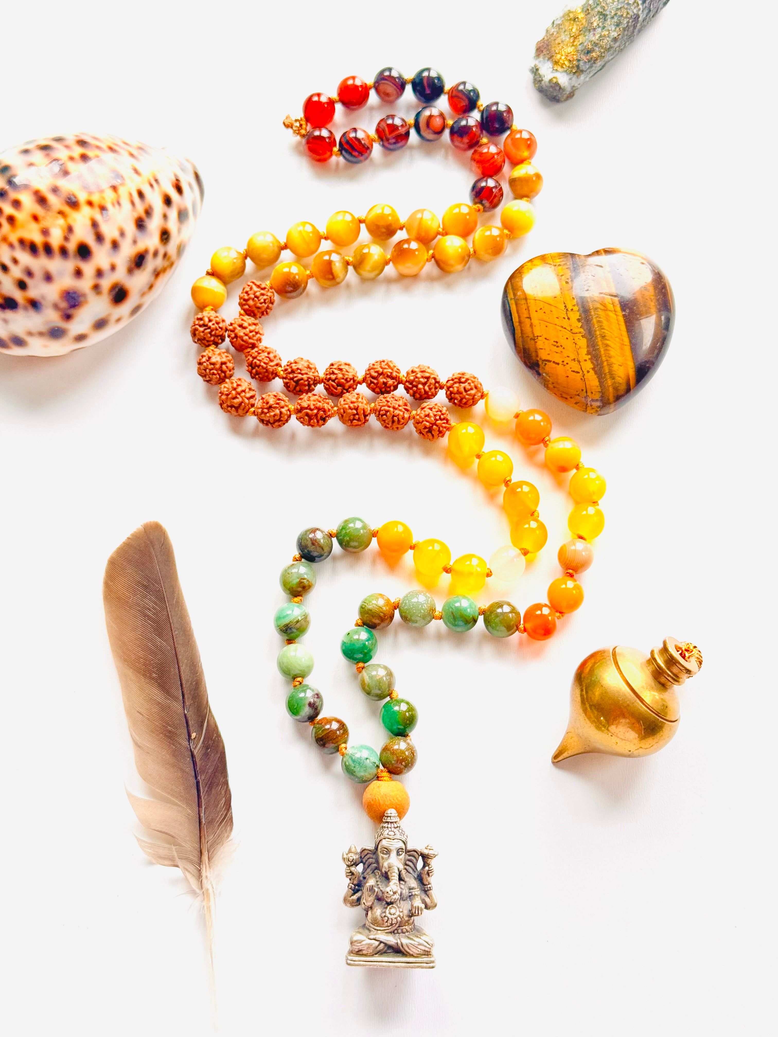 Colorful beaded necklace with a pendant, surrounded by shells and a feather on a white background