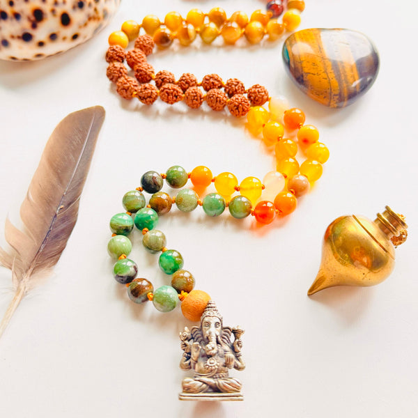 Colorful beaded necklaces with a Ganesha pendant, shell, feather, and stones on a white background