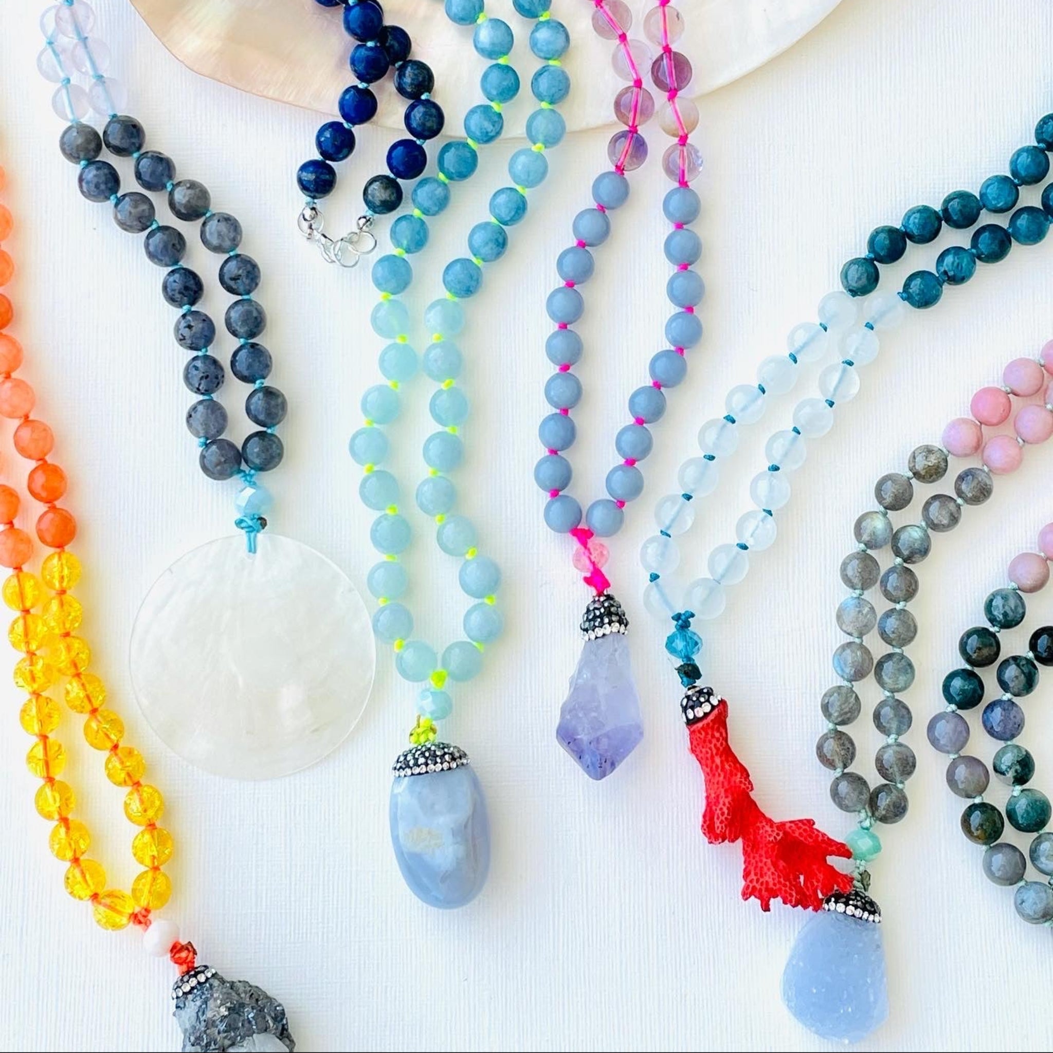 Colorful beaded necklaces on a white surface with seashells.