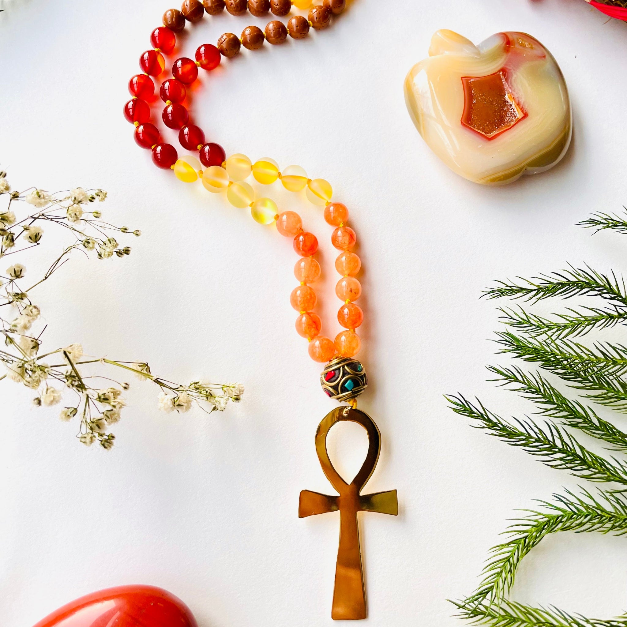 A colorful beaded necklace with a gold-plated ankh pendant, displayed against a background of decorative elements.
