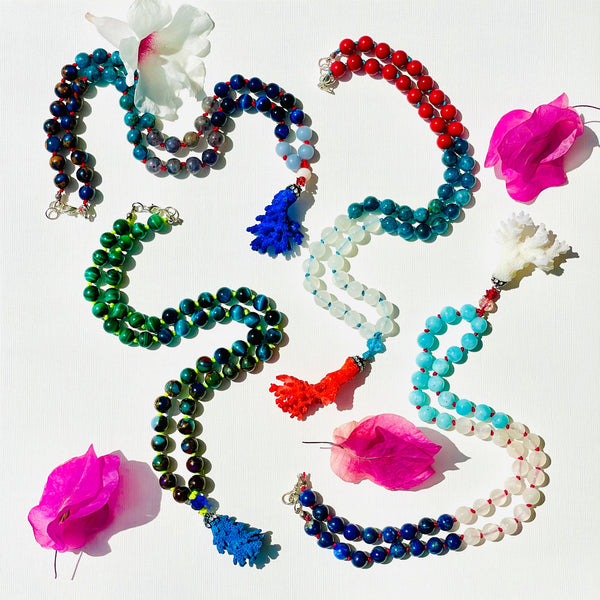 Colorful beaded necklaces on white surface and pink flowers