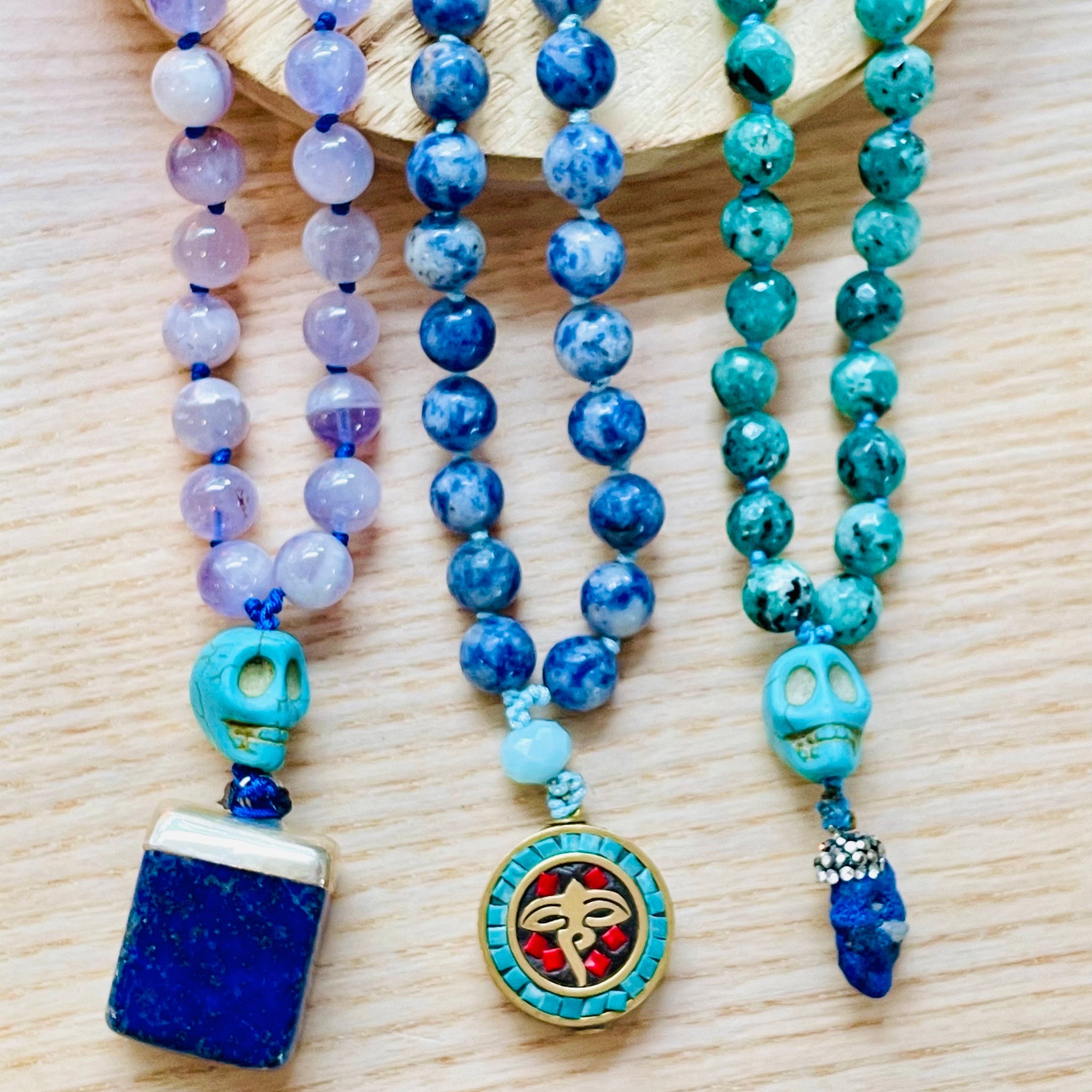 Three beaded necklaces with colorful beads and decorative pendants on a wooden surface.