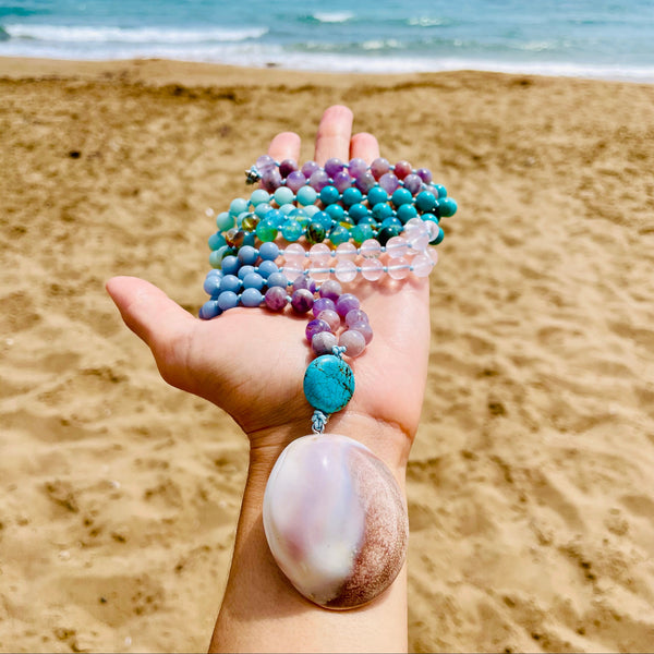 blue white and purple beaded mala with shell pendant photo near the beach and sand