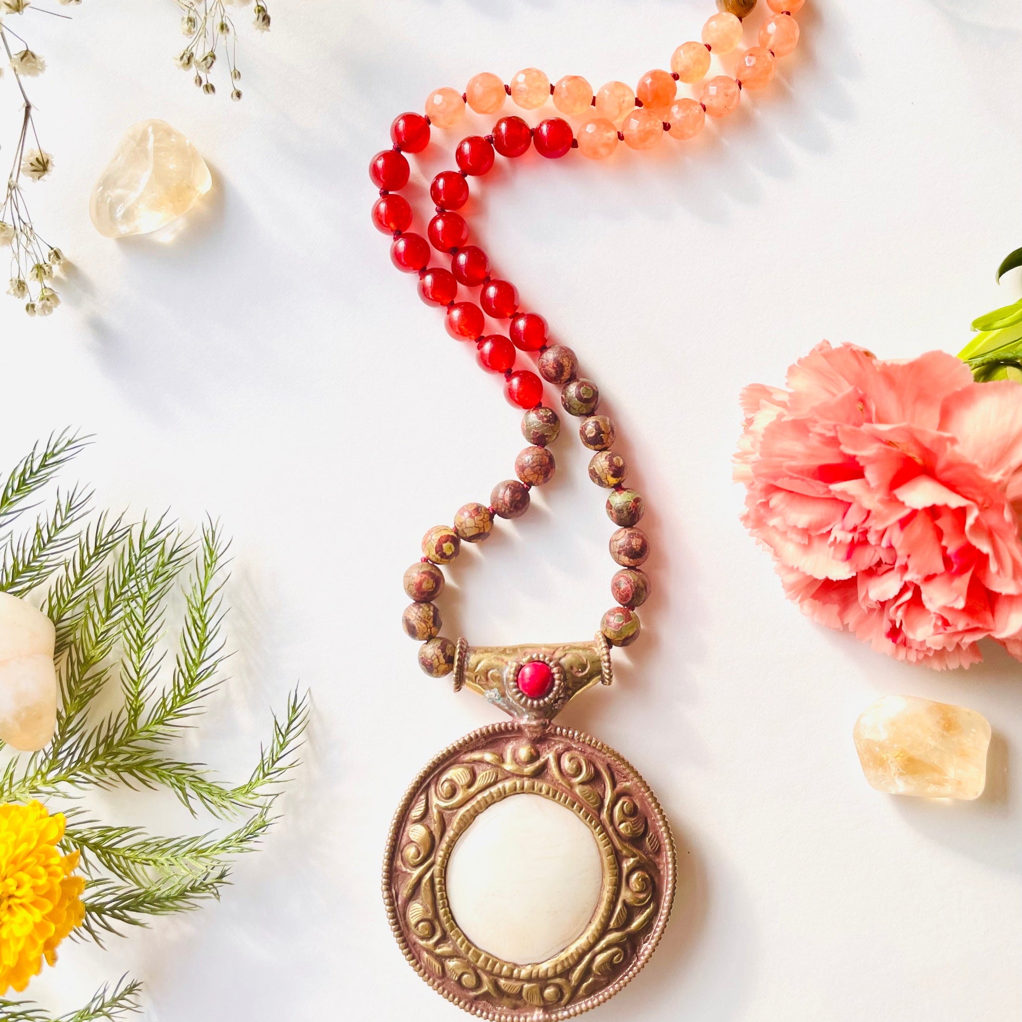 A close-up image of a Focused & Motivated Necklace with a vintage brass pendant, featuring a series of round beads with varying hues and a chain.