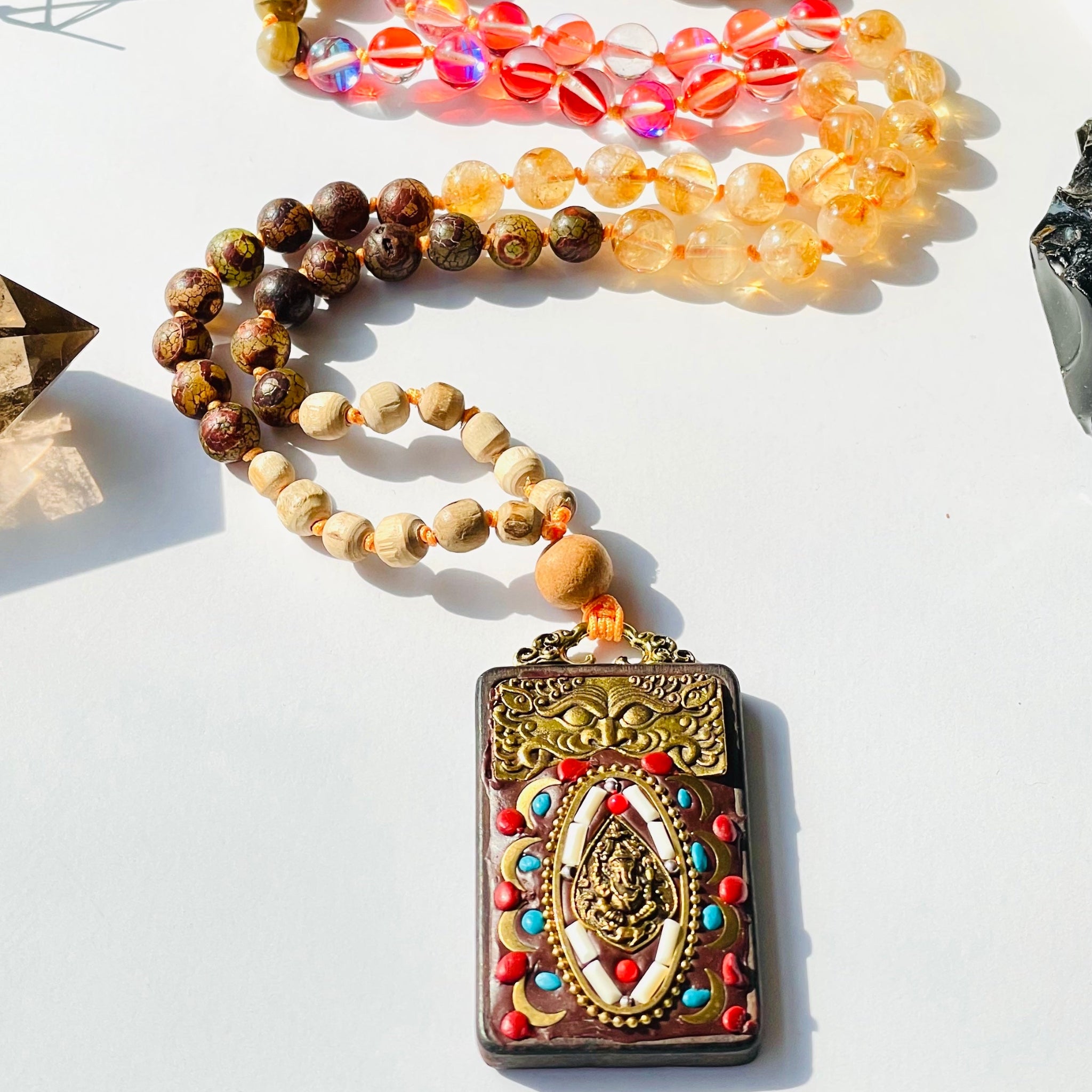 A variety of spiritual beads and gemstone necklaces laid out, featuring a prominent vintage Nepal wood beaded Ganesh pendant.