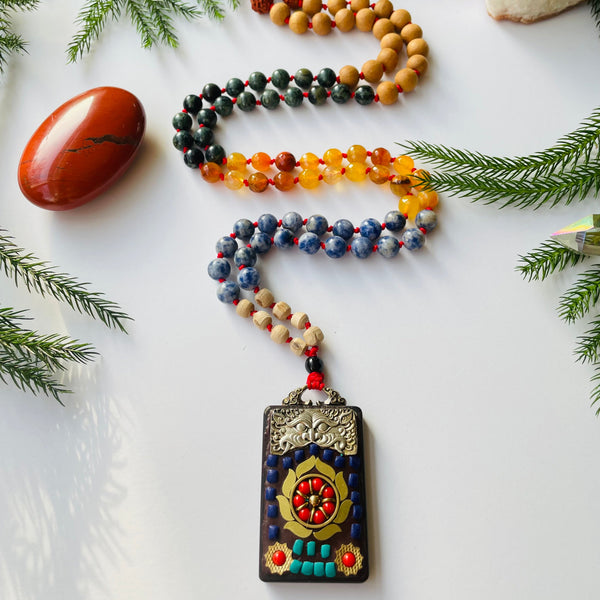 A multicolored beaded mala with a Ganesha bead accent, featuring a red knot and a metal pendant with a Ganesha image.