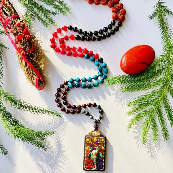 blue red and black gemstones beaded with elephant wood carved pendant on white surface with pine needles