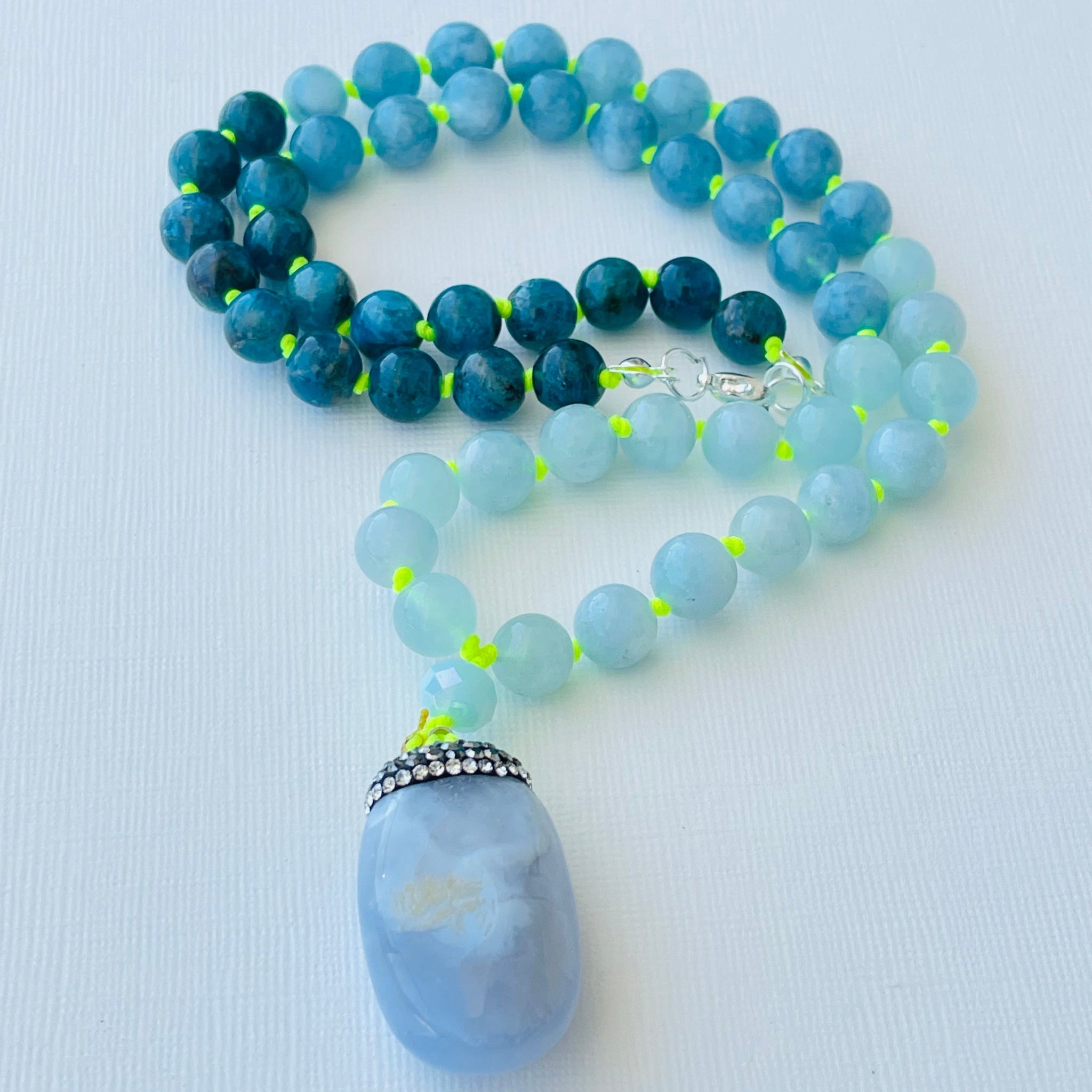 A beaded necklace with a chalcedony pendant, featuring blue and green gemstone beads, and a silver-colored mala pendant.