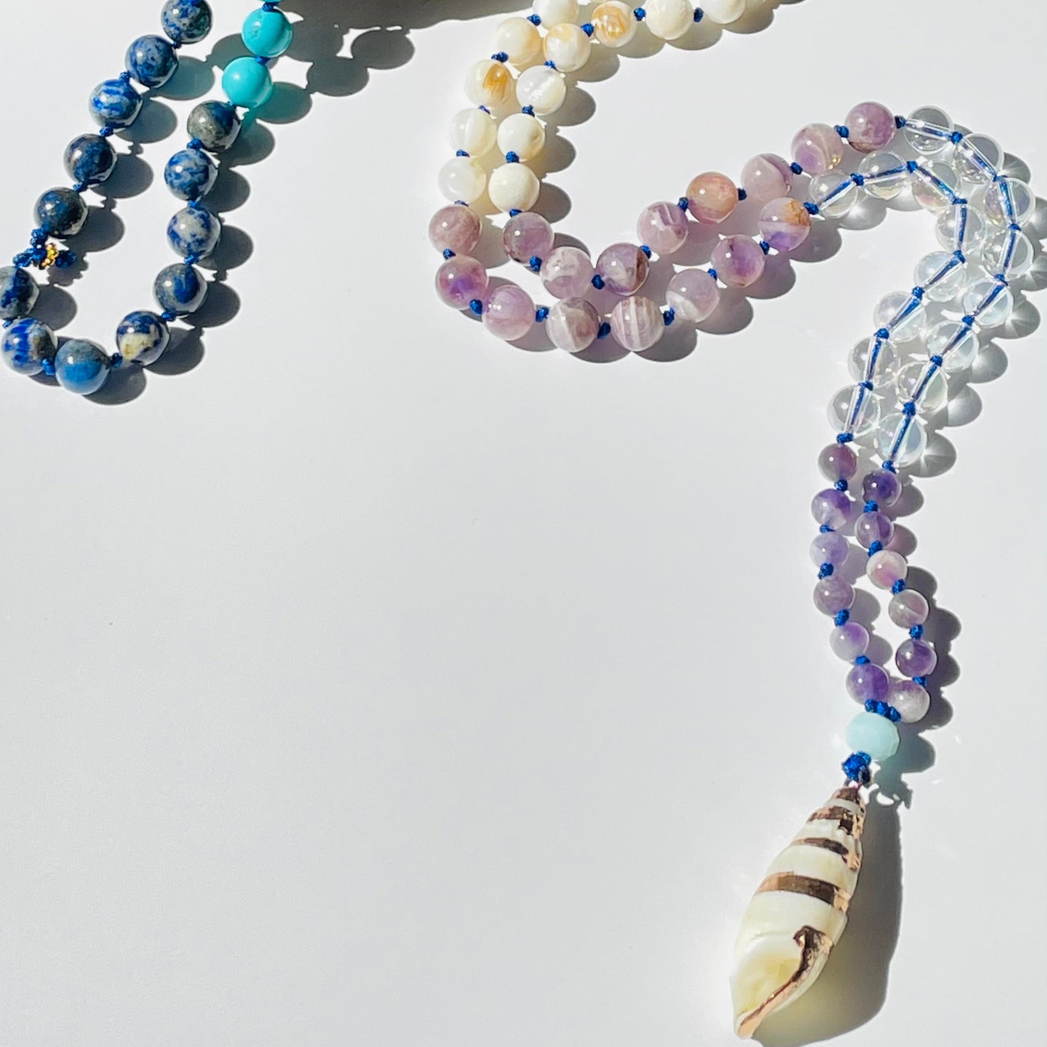beaded gemstone necklace with seashell pendant on white surface
