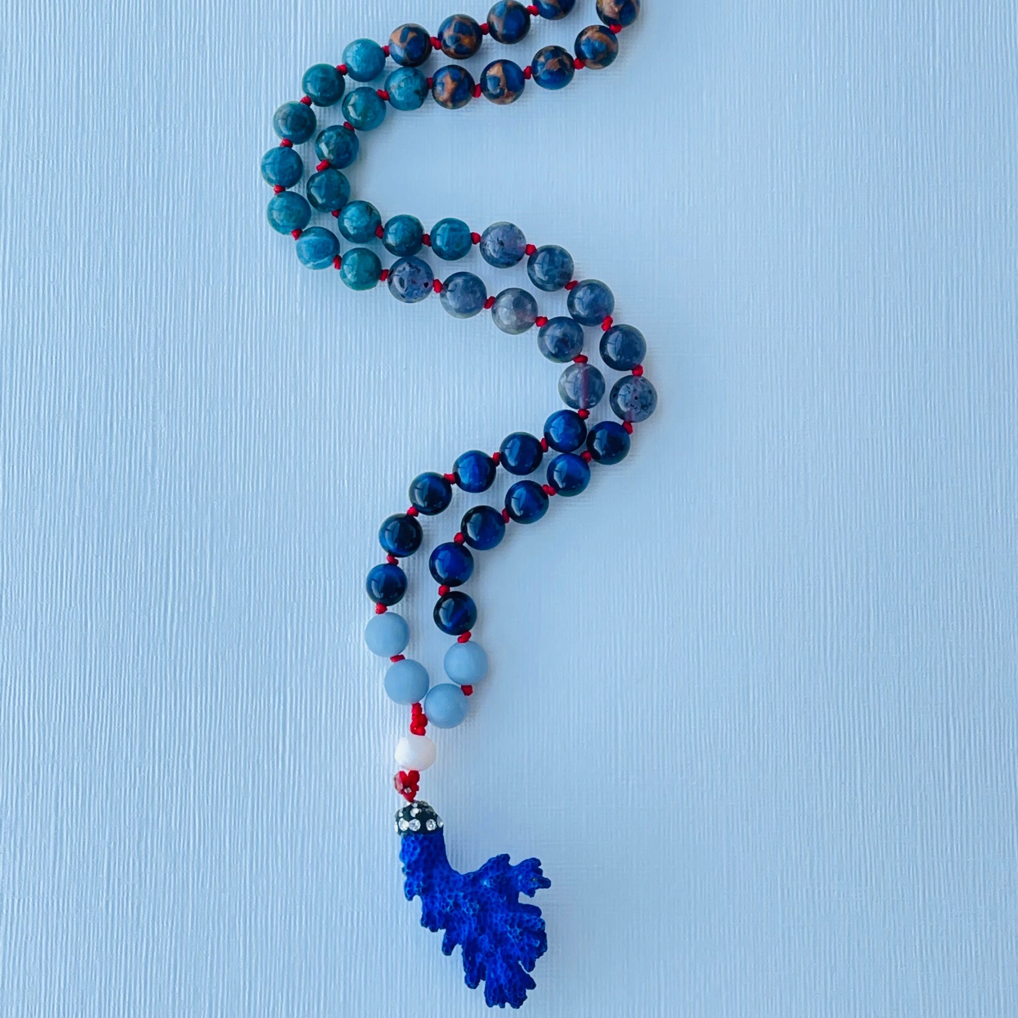 Beaded necklace with a blue pendant on a light blue background