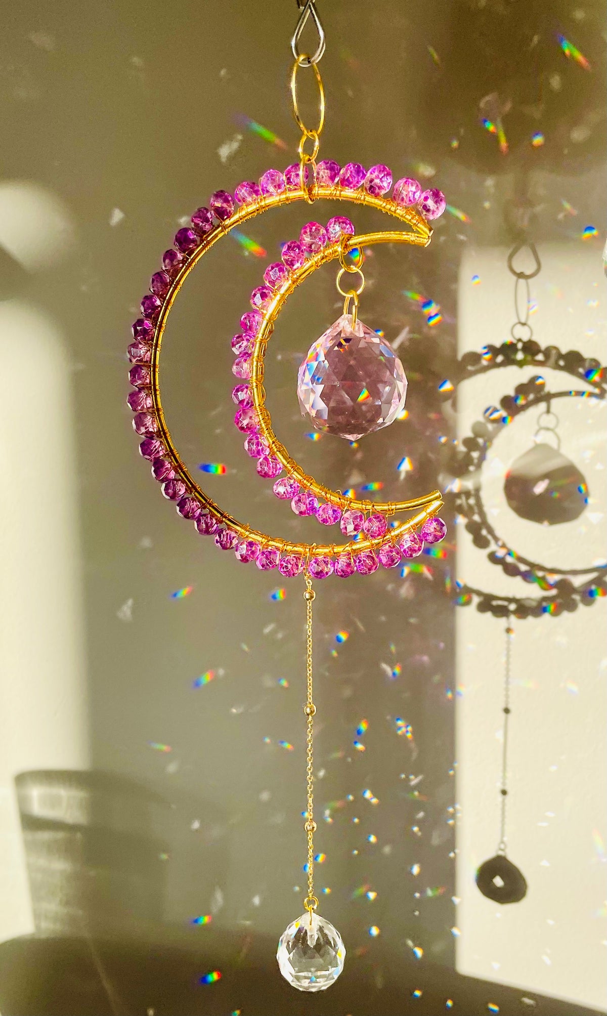 A crescent-shaped suncatcher with lilac pink crystals and a central orange crystal, hanging from a metallic loop.