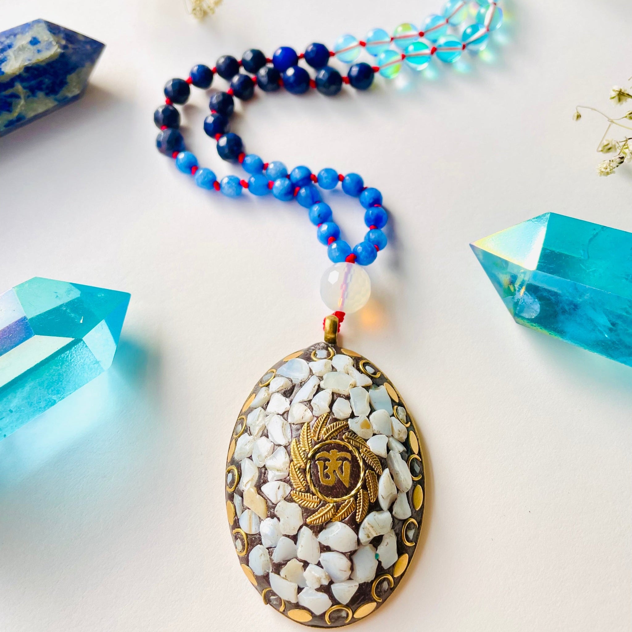 Blue gemstone beaded necklace on red string with big brass pendant that has white gemstones 