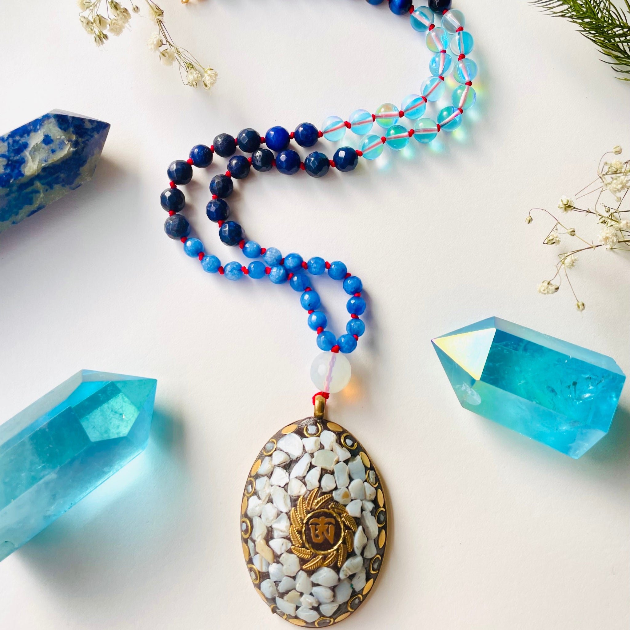 Blue gemstone beaded necklace on red string with big brass pendant that has white gemstones 