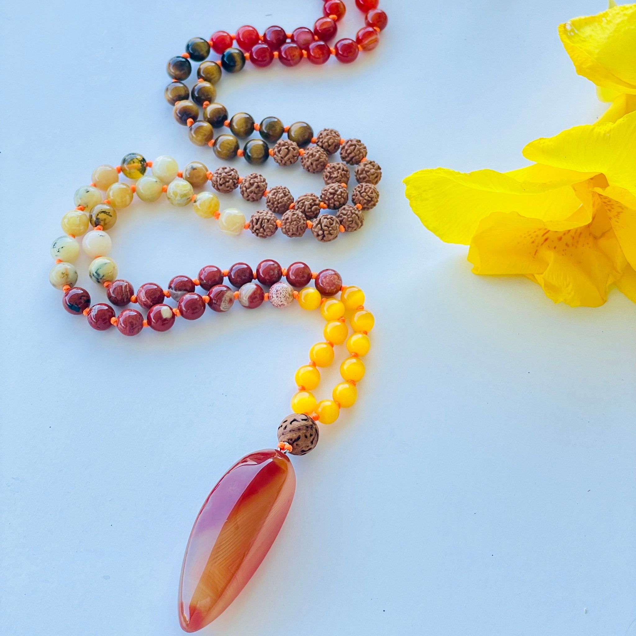Beaded necklace with brown, yellow, red beads with orange gemstone pendant and yellow decorative flowers