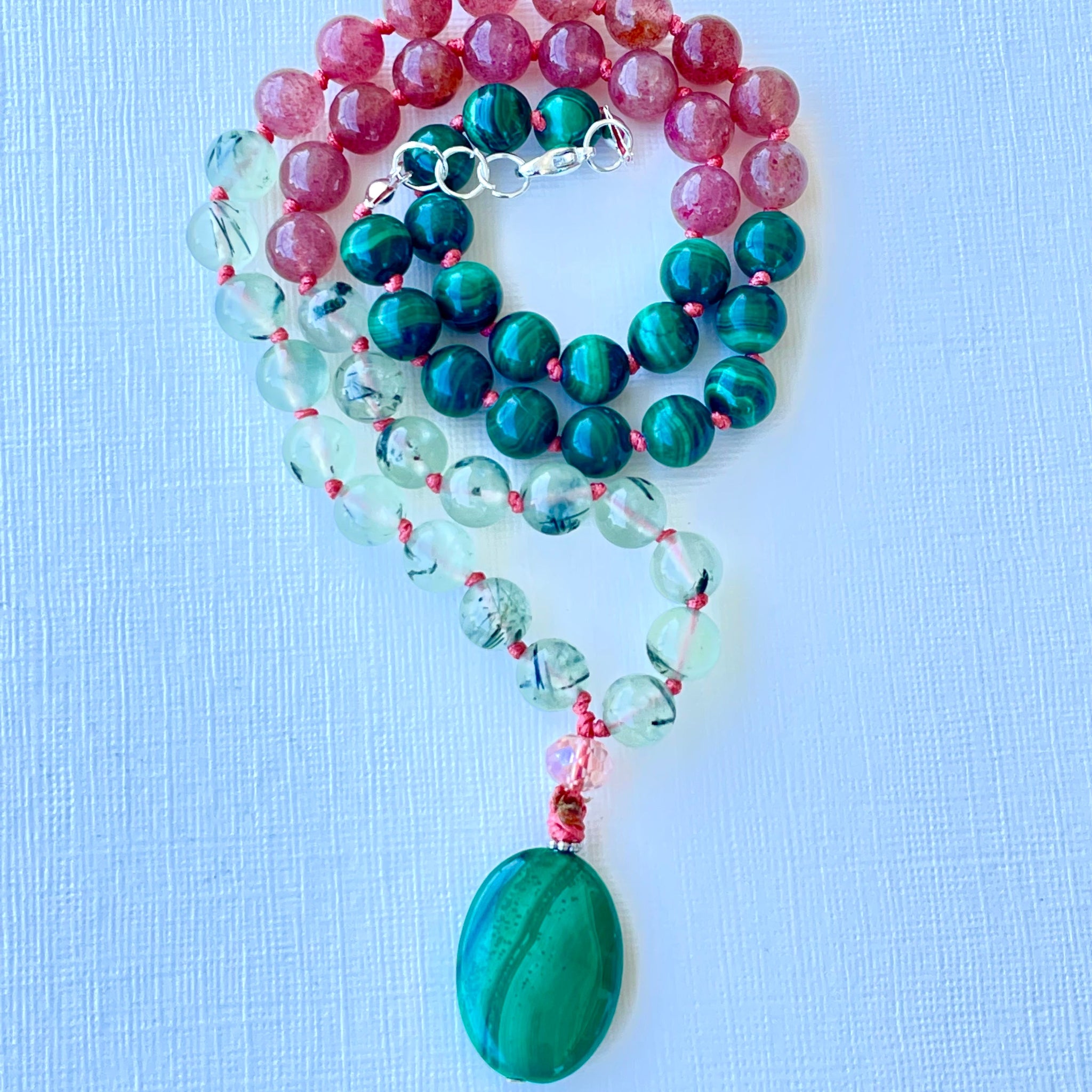 A beaded necklace with a green pendant, featuring a mix of pink, green, and clear beads, and a silver cap and chain.
