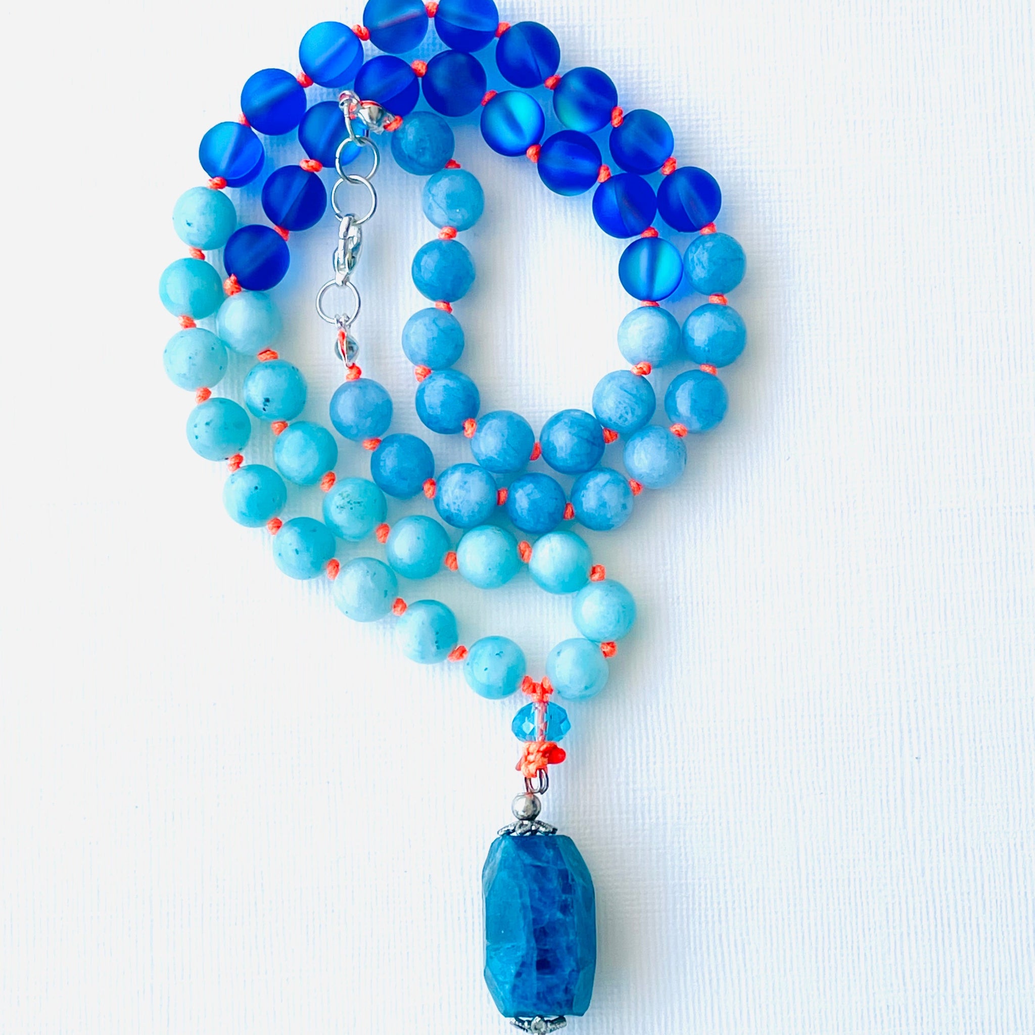 A blue and orange beaded necklace with a pendant, likely to be used for spiritual practices.