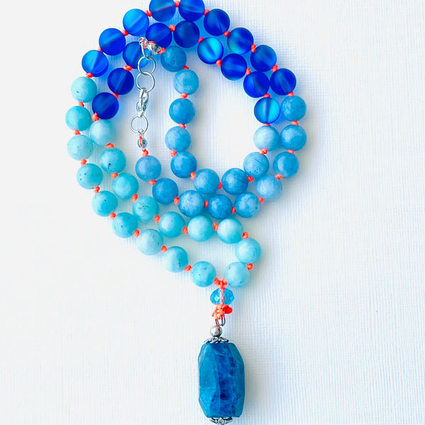 A blue and orange beaded necklace with a pendant, likely to be used for spiritual practices.
